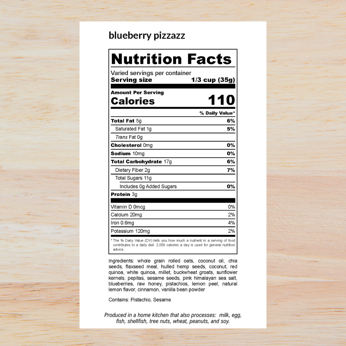 A white nutrition facts label for 'blueberry pizzazz' displayed on a light wood background, with product name, serving size, calories, nutrients, ingredients, and a small production note printed on it.