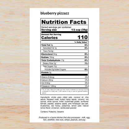 A white nutrition facts label for 'blueberry pizzazz' displayed on a light wood background, with product name, serving size, calories, nutrients, ingredients, and a small production note printed on it.