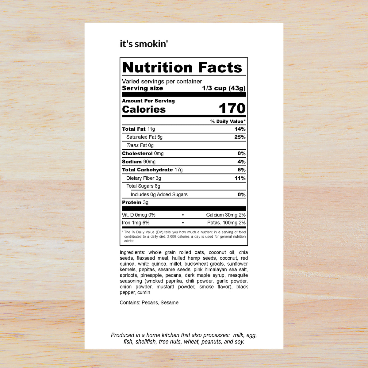 A Nutrition Facts label for a snack mix on a light wood background. The label reads 'it's smokin'' at the top and shows 170 calories per serving with a detailed breakdown of nutrients and ingredients listed below.